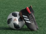 black adidas cleats lean on white and black adidas soccer ball on green grass