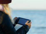 a woman holding a game controller in front of a body of water