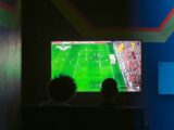 Two people watching a soccer game on a television