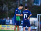 Two soccer players in blue jerseys strategize during a match in Hà Nội, Vietnam.