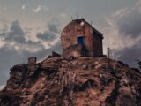 An old brick structure perched on a rocky hill, amidst a dramatic cloudy sky.