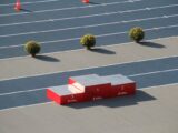 Red podium on a sunny outdoor athletics track with decorative plants.