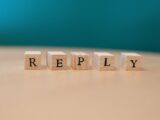 Close-up of wooden blocks spelling 'REPLY' on a table with teal background.