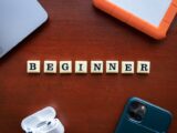 A top view of beginner workspace items including gadgets and letter dice on a wooden desk.