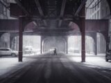Person crossing a snowy street under elevated train tracks.