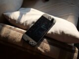 A handheld gaming console rests on pillows.