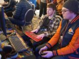 man using video game control pad beside man using computer keyboard sitting and playing video games
