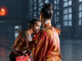 A dramatic scene of martial artists in traditional Japanese attire poised in confrontation within an industrial setting.