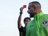 A man in a green hoodie holding up a red card