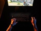 A gamer intensely playing a first-person shooter game on a computer setup indoors at night.