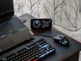 A modern workspace featuring a laptop, digital clock, gaming mouse, and keyboard, ideal for work and tech enthusiasts.